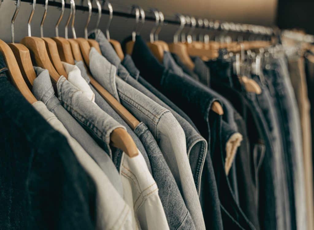 Clothing racks filled with various denim and casual jackets on wooden hangers, displayed in a clothing manufacturing or retail setting.