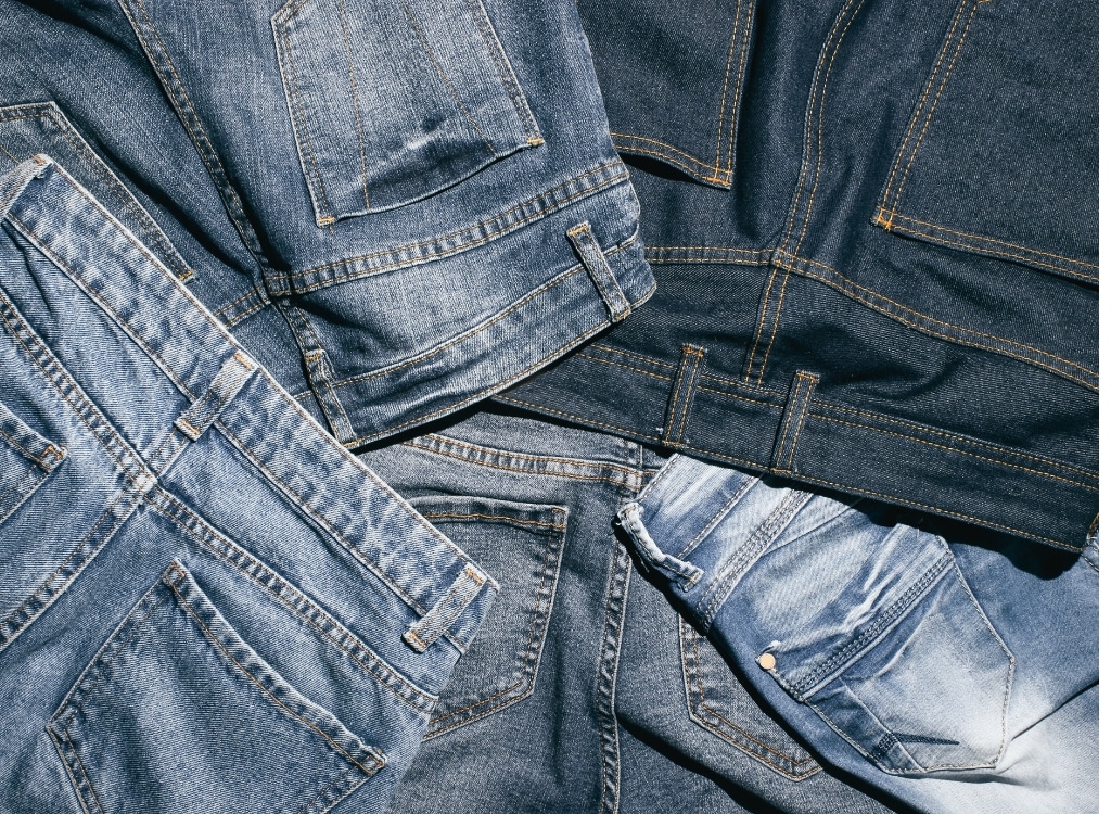 Close-up image of multiple denim jeans in various shades, showcasing different styles and stitching details.