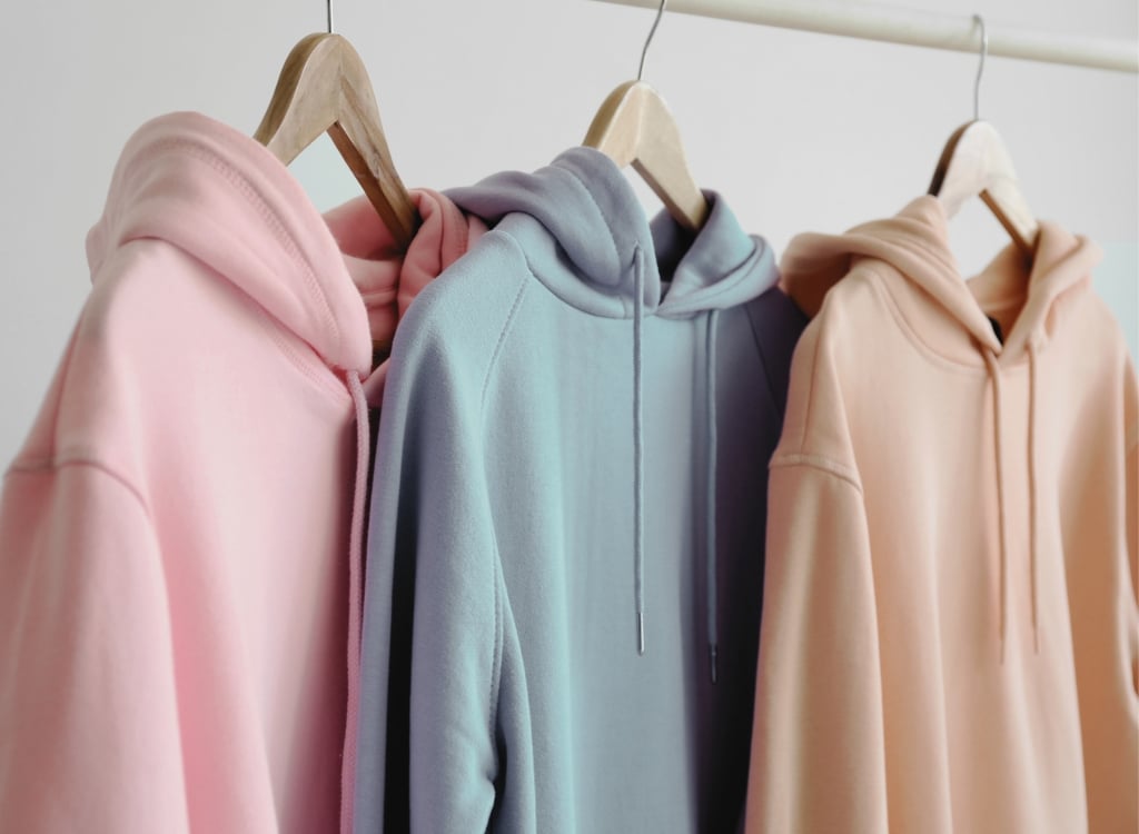 Colorful pastel hoodies hanging on wooden hangers on a clothing rack.