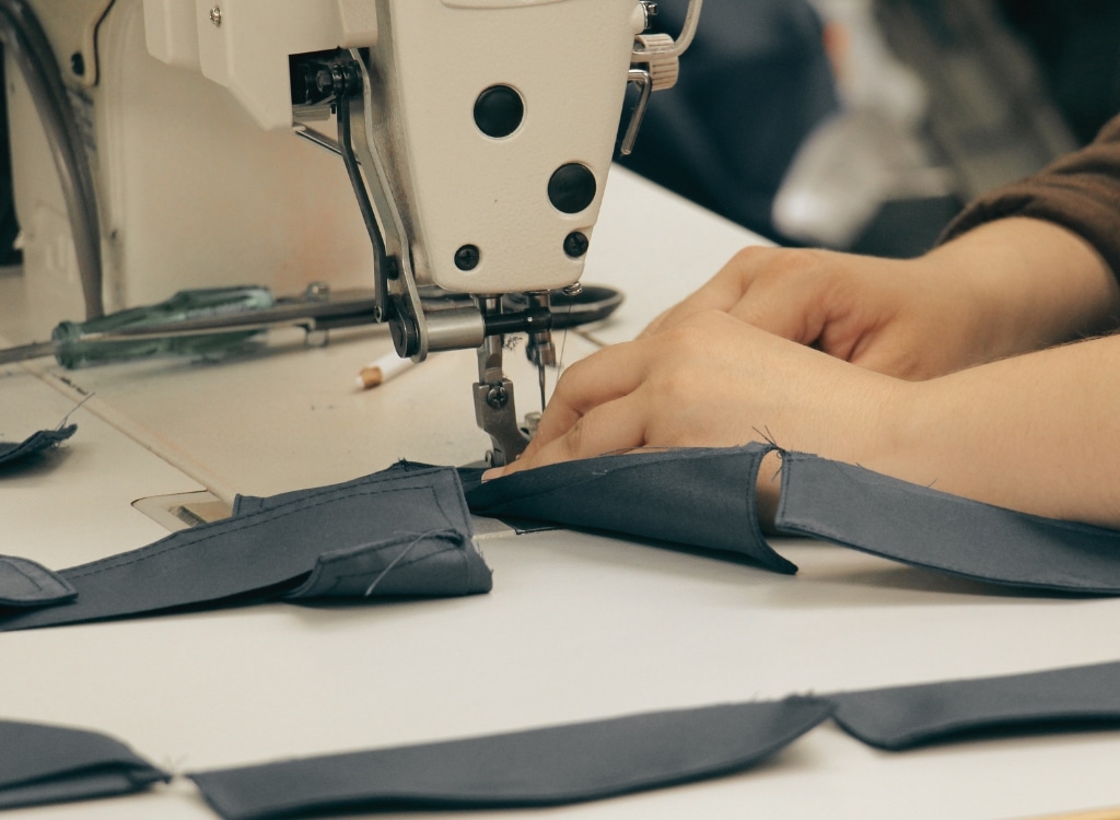 A close-up of a person sewing fabric on a sewing machine in a clothing manufacturing workshop in Minnesota.