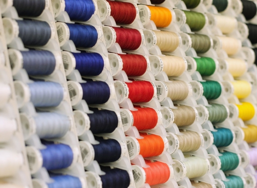 Spools of colorful sewing thread arranged on a rack at a clothing manufacturing facility.