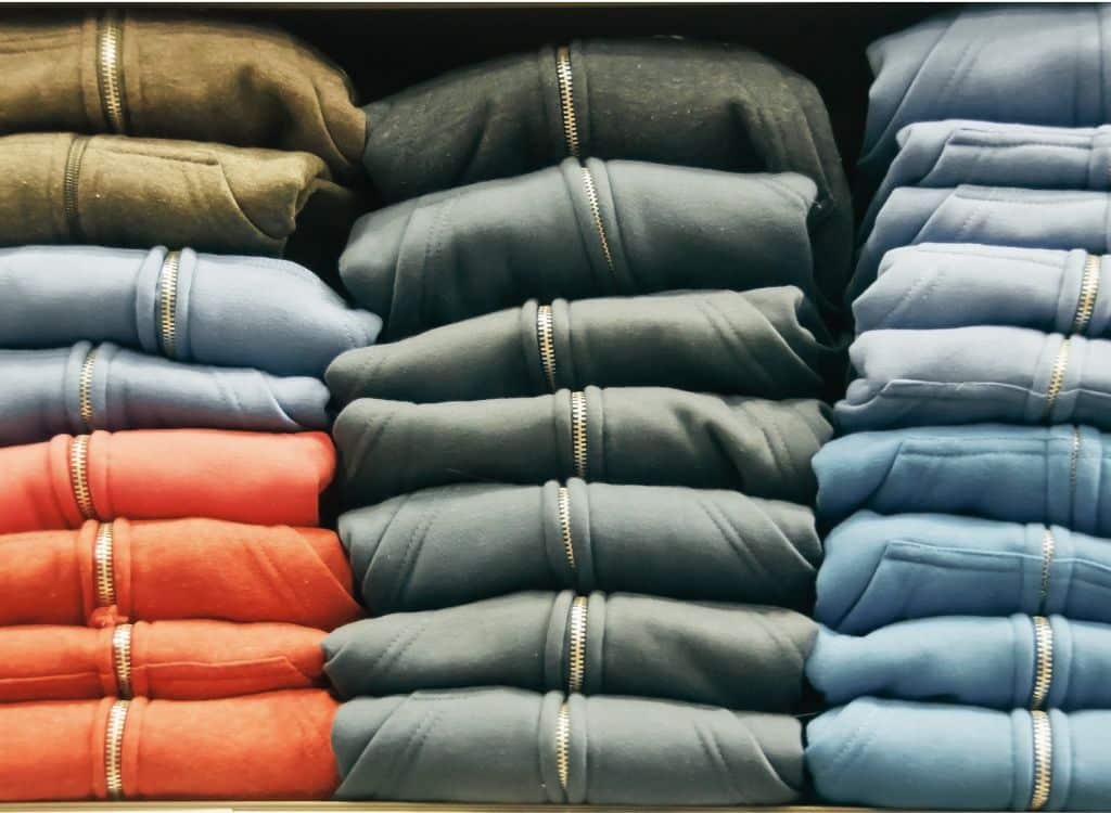 Stacks of folded jackets in various colors with zippers, arranged neatly on a shelf.