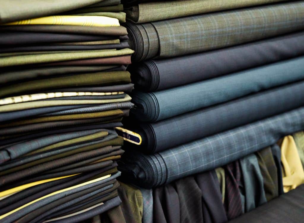 Stacked rolls of fabric in various patterns and colors at a clothing manufacturing facility.