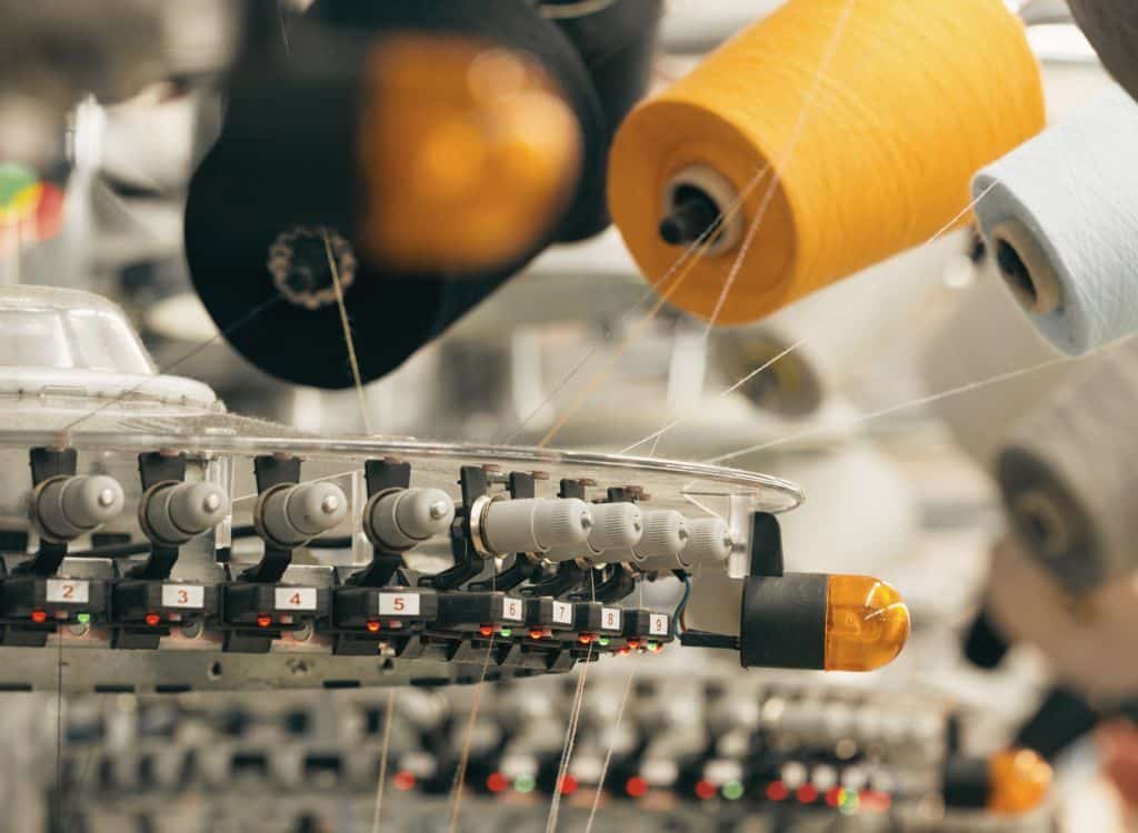 Close-up of industrial textile machinery with colorful yarn spools at a clothing manufacturing facility in Rhode Island