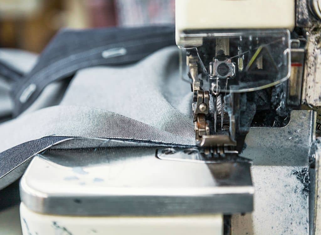 Close-up of an industrial sewing machine stitching denim fabric at a clothing manufacturer in Rhode Island.