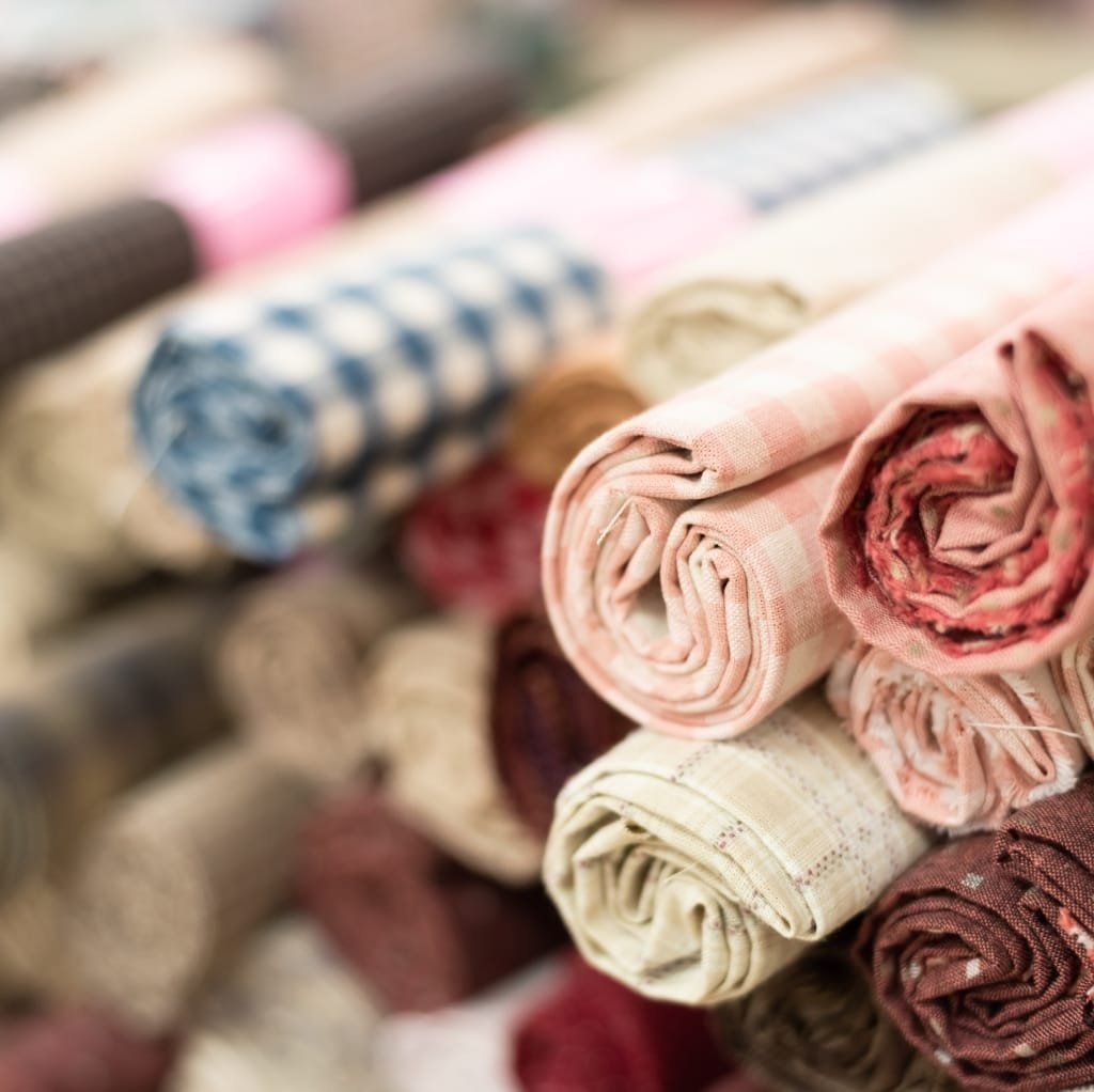 Rolled-up bundles of various patterned and colored cotton fabrics arranged on a display shelf, suggesting a wholesale fabric store.