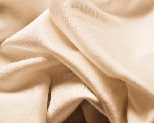 Close-up view of cream-colored, soft cotton fabric with gentle folds and smooth texture.