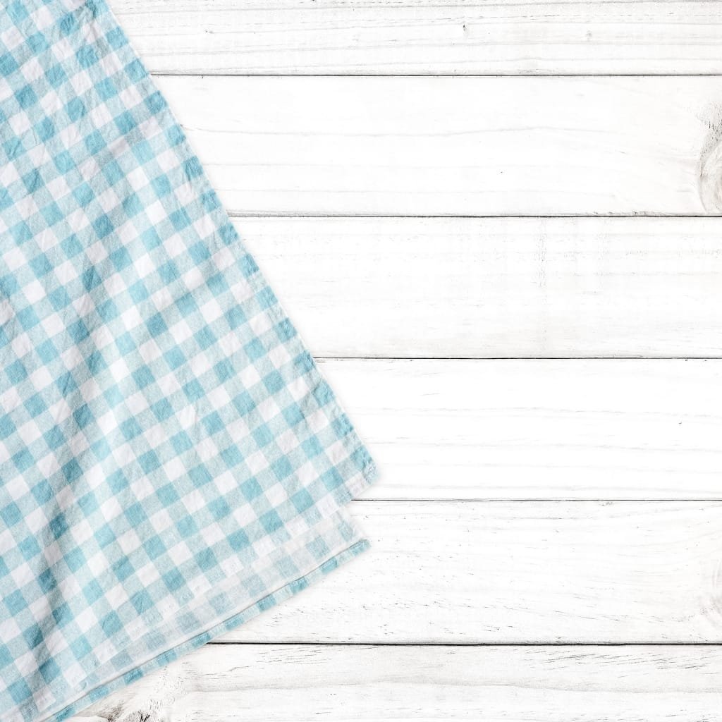 Light blue and white checkered cloth partially folded on a white wooden surface.
