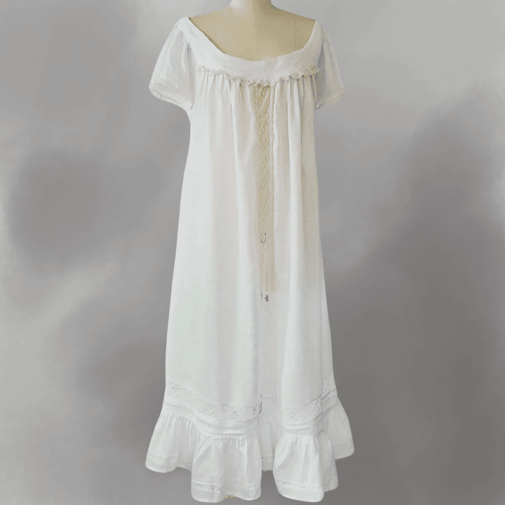 A vintage-style white nightgown with short sleeves, featuring lace and ruffle details, hanging against a plain gray background.