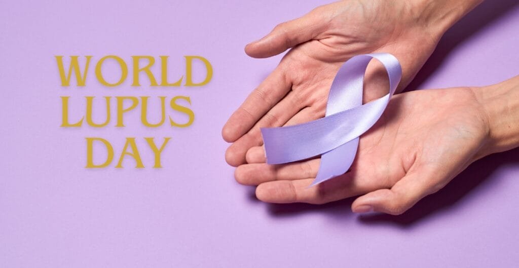 Hands holding a lavender ribbon symbolizing World Lupus Day against a light purple background, with the text "World Lupus Day" in yellow on the left.