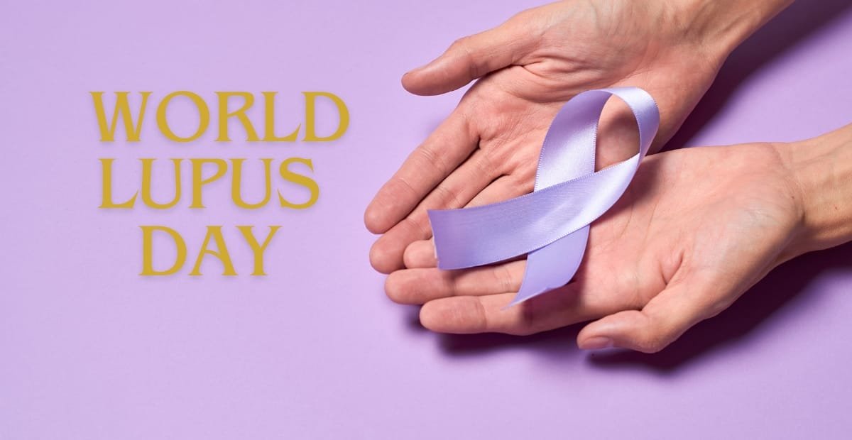 Hands holding a lavender ribbon symbolizing World Lupus Day against a light purple background, with the text "World Lupus Day" in yellow on the left.