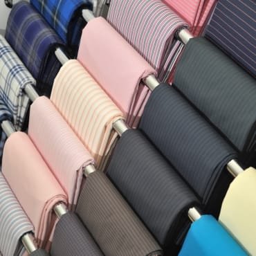 A display of polyester fabric rolls in various colors and patterns, including stripes and solids, arranged on a rack.