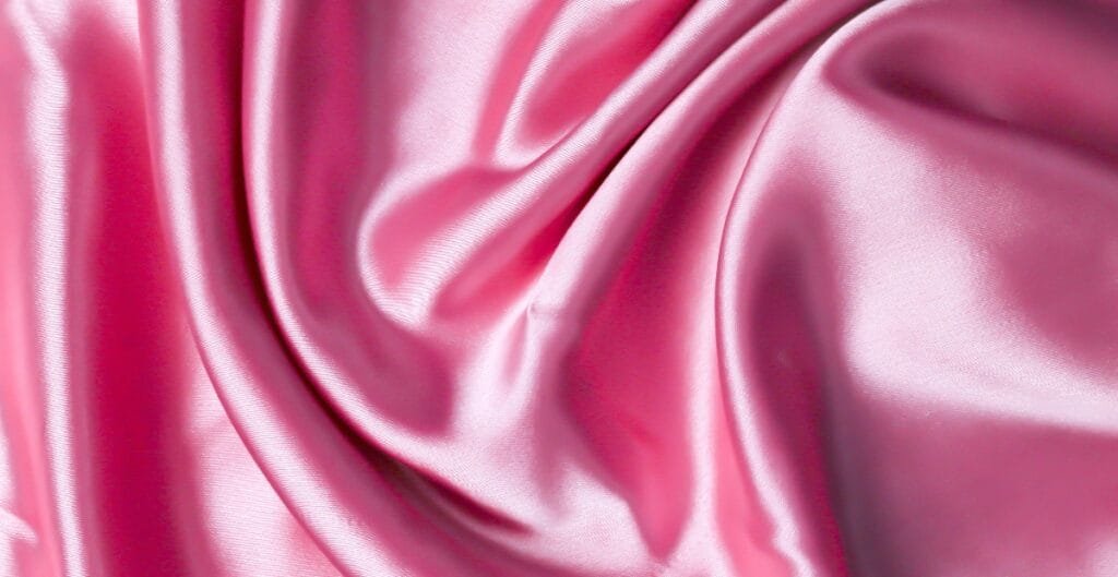 Close-up image of pink, shiny, and smooth breathable polyester fabric with gentle folds.