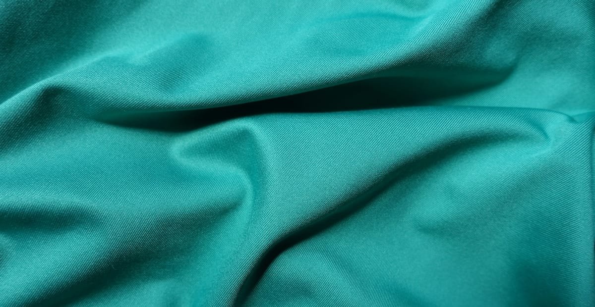Close-up image of teal brushed polyester fabric, showcasing a smooth and slightly textured surface suitable for casual wear.