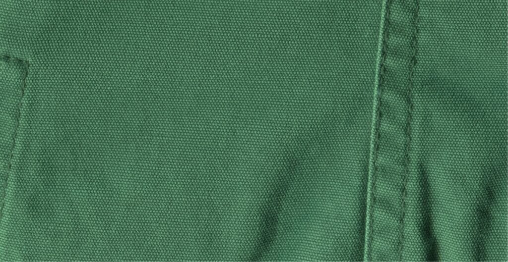 Close-up image of green cotton chambray fabric showing its tightly woven texture and faint diagonal weave pattern.