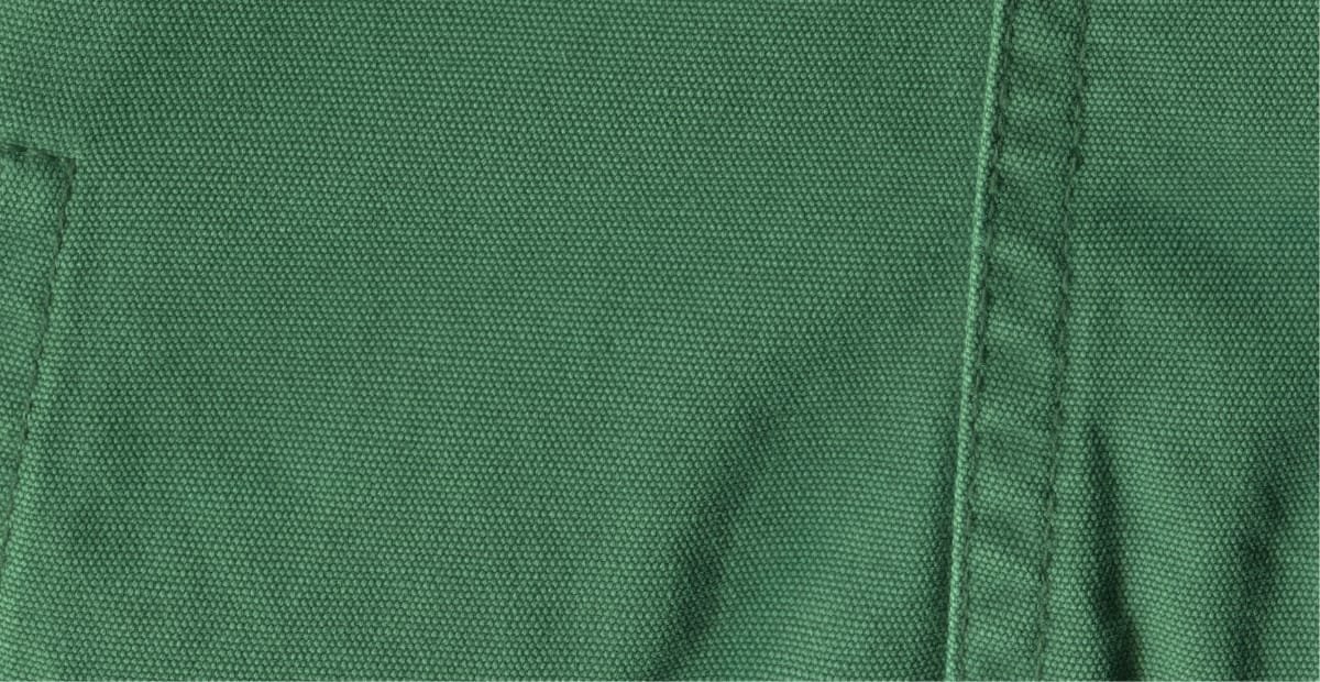 Close-up image of green cotton chambray fabric showing its tightly woven texture and faint diagonal weave pattern.