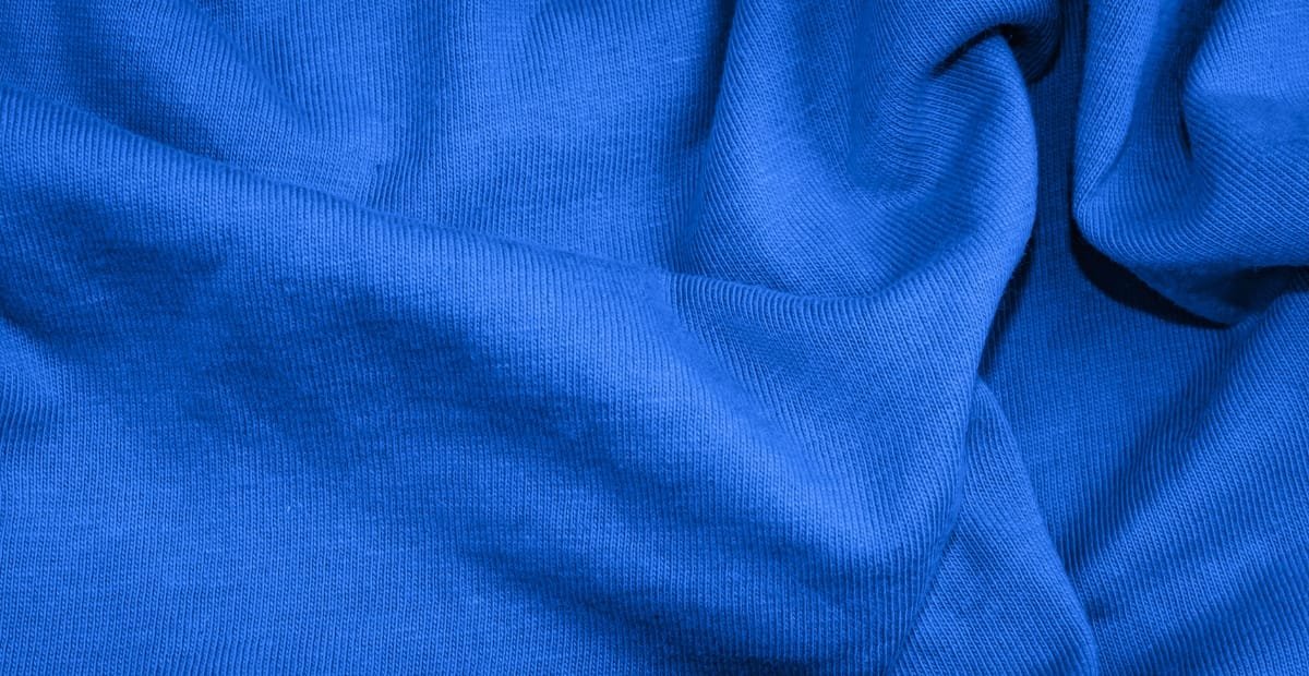 Close-up image of blue fabric with visible weave texture and folds, made from a cotton-polyester blend.