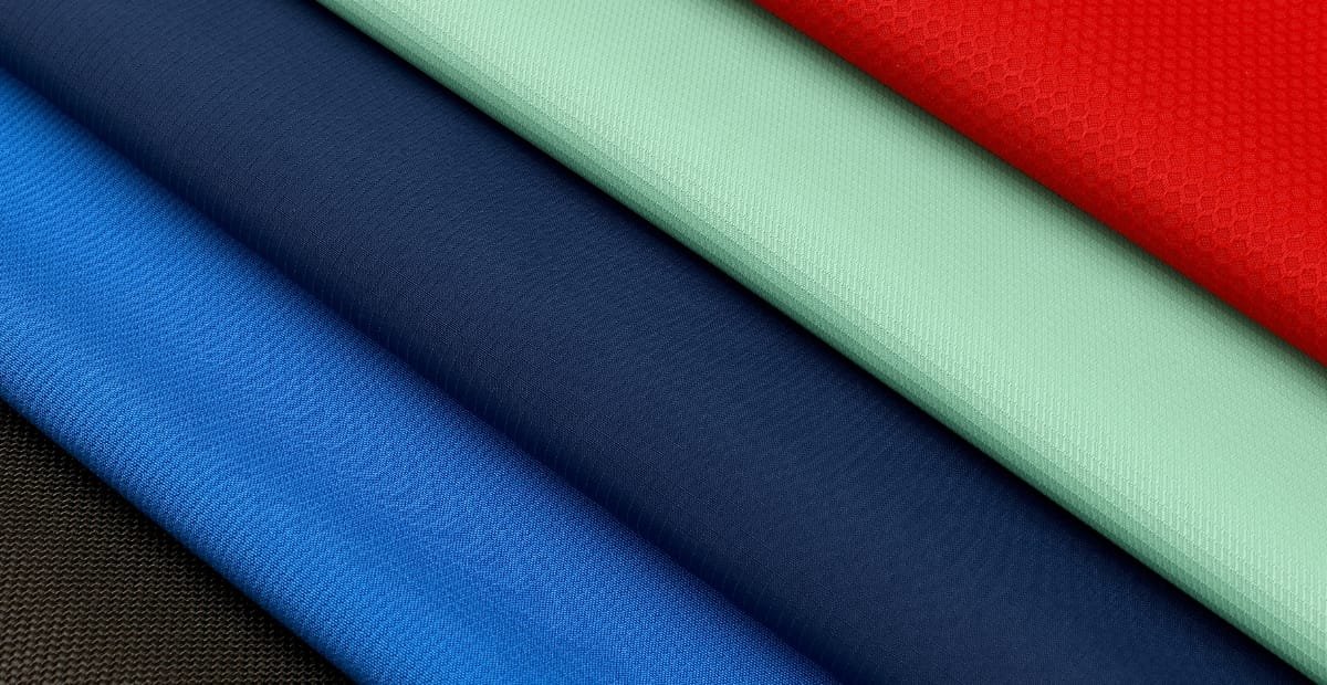 Folded lightweight polyester fabric in various colors including red, green, navy blue, royal blue, and black.