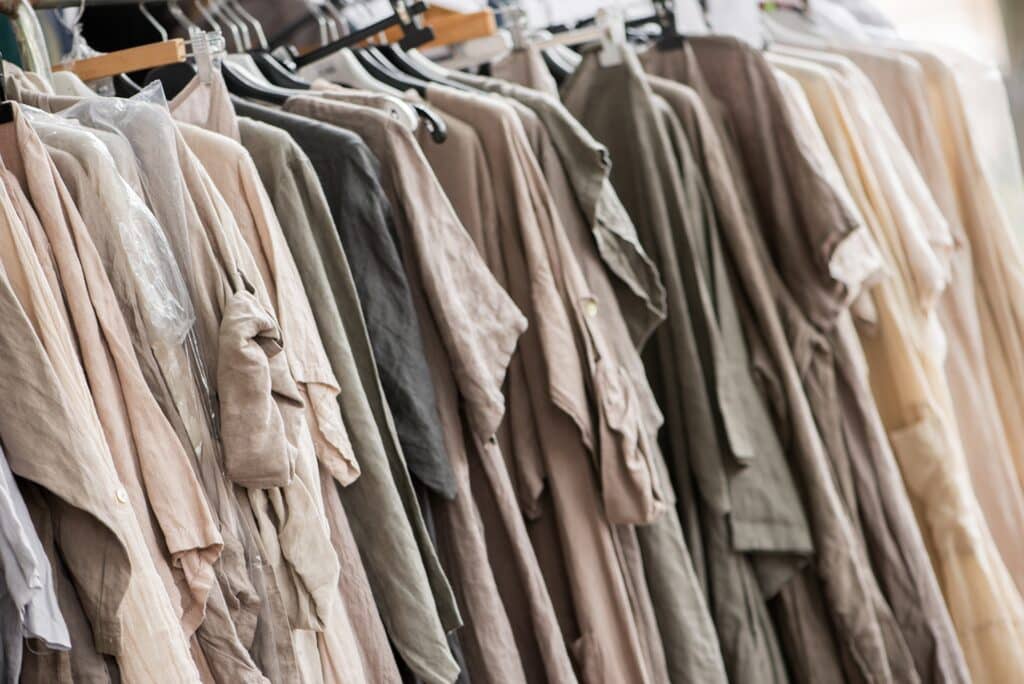 A row of neatly arranged beige, gray, and neutral-colored shirts hanging on a clothing rack, representing apparel manufacturing.