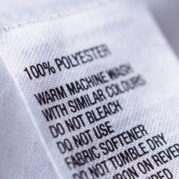 Clothing label with care instructions for 100% polyester, including washing, bleaching, and fabric softener guidelines.
