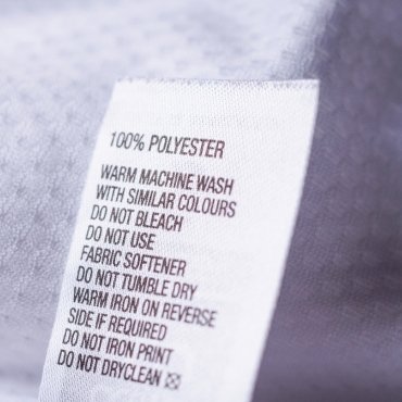 Clothing label indicating care instructions for 100% polyester fabric, including washing, drying, and ironing guidelines.