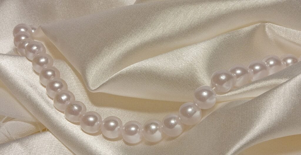 A pearl necklace resting on a smooth, satin-like fabric with a silky sheen and soft folds.