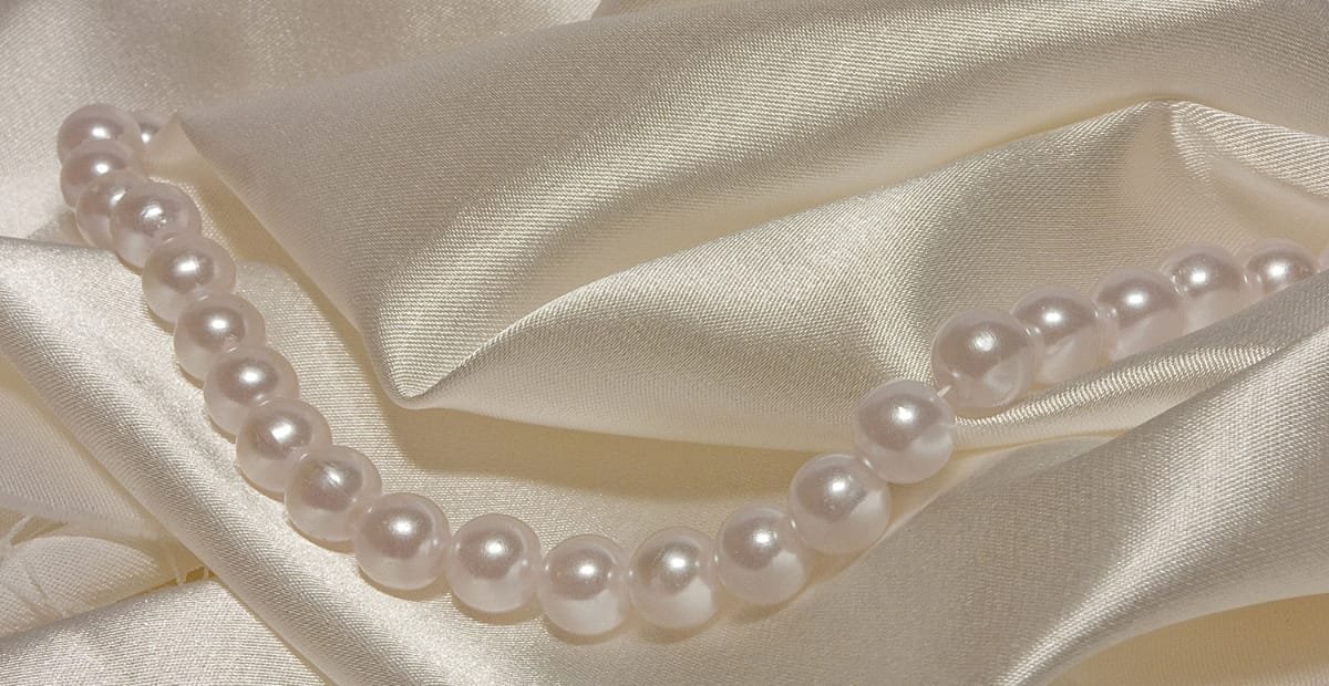 A pearl necklace resting on a smooth, satin-like fabric with a silky sheen and soft folds.