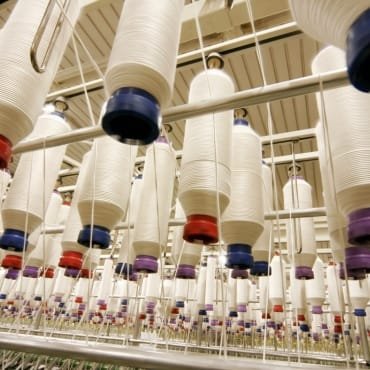 Multiple large spools of PET polyester yarn hanging in a textile manufacturing facility, arranged in rows.