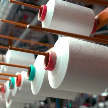 Close-up of large spools of PET polyester yarn mounted on an industrial reel, with the yarn appearing smooth and white.