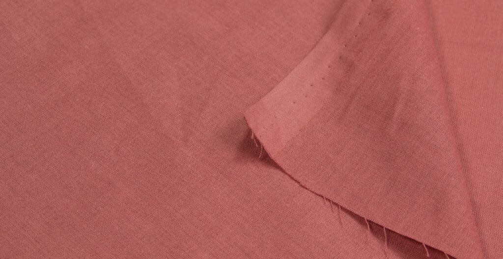 A close-up image of a pink poplin cotton fabric, showing the texture and weave of the material with a folded edge.