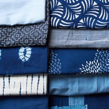 Collection of folded fabrics featuring various blue and white patterns, including geometric, abstract, and striped designs.