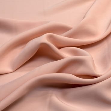 Soft, flowing fabric in a light peach color with gentle folds and smooth texture, showcasing a polyester-rayon blend.