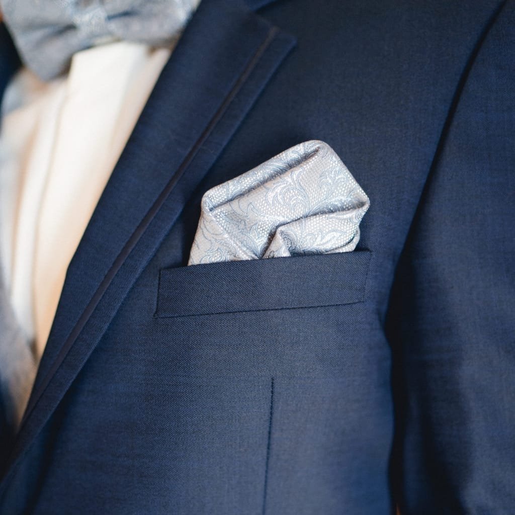 A silver pocket square with an intricate paisley pattern tucked neatly into the breast pocket of a dark blue suit jacket.