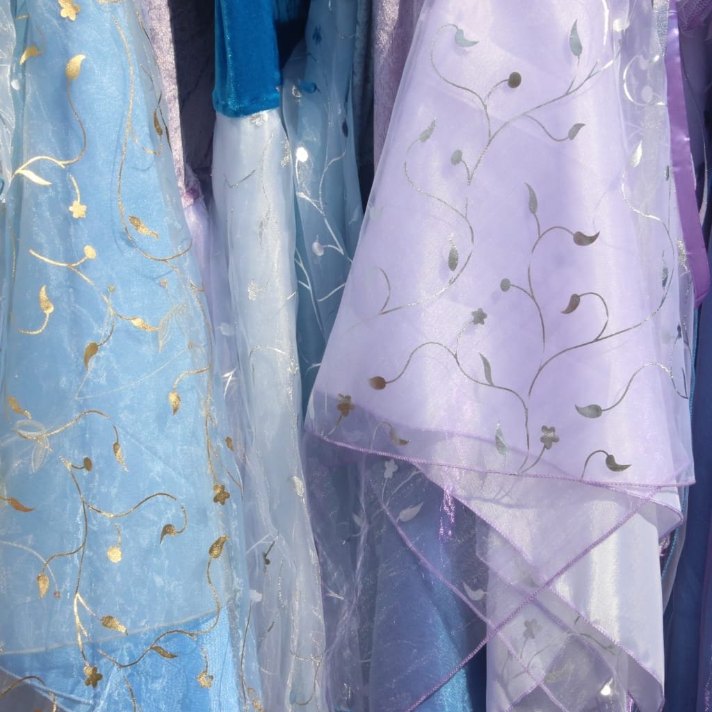 Close-up image of elegant, semi-transparent fabrics in pastel shades (light blue, lavender, and white) with gold embroidered floral and vine patterns. The fabrics have a delicate, flowy appearance, showing intricate embroidery and lightweight, soft drape qualities.