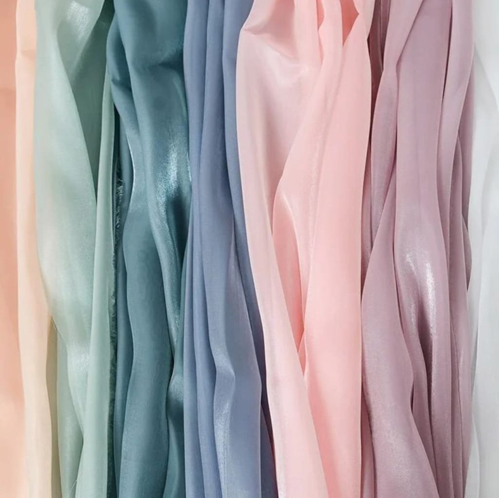 A close-up image of pastel-colored cotton chiffon fabric, featuring shades of mint green, teal, light purple, soft pink, lavender, and beige.