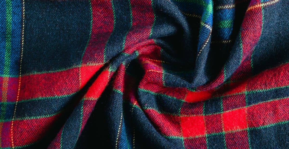 Close-up image of a piece of brushed cotton fabric with a tartan plaid pattern in red, green, and navy blue colors.