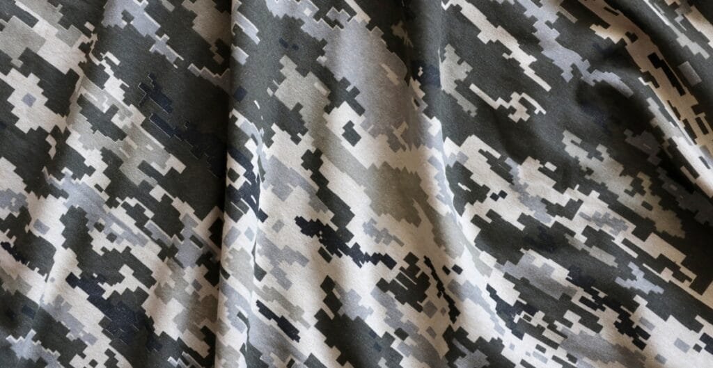 A close-up image of a fabric with a digital camouflage pattern in shades of gray, black, and beige.