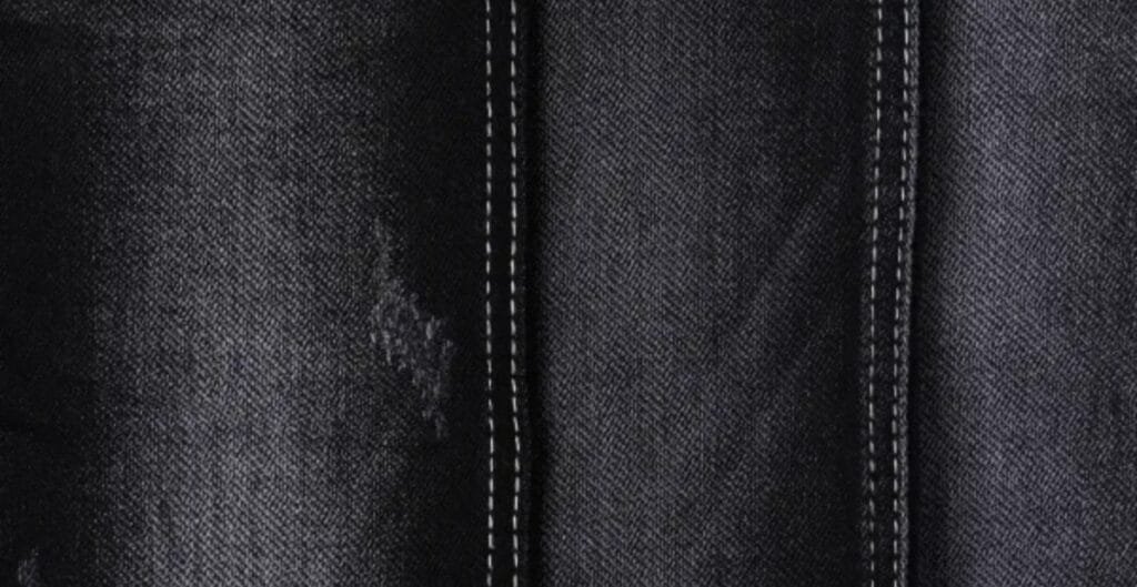 Close-up of black denim fabric with subtle texture, showing tight weave and tiny white specks, highlighting the fabric’s rich color.