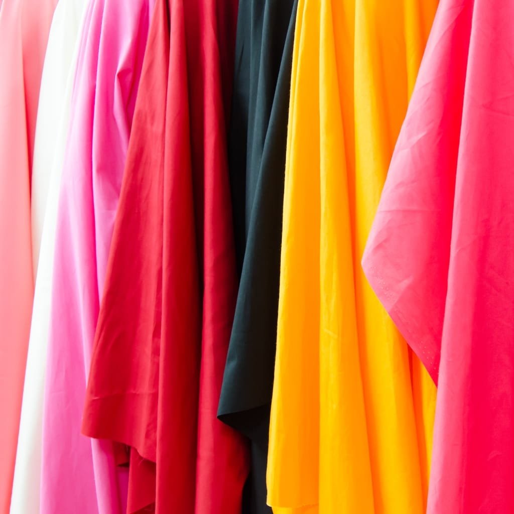 Rows of colorful fabric hanging side by side, including shades of pink, red, black, and yellow.