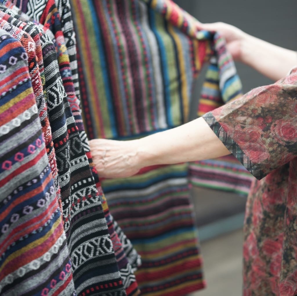 Close-up of hands touching and inspecting vibrant, woven cloth with colorful, intricate patterns, highlighting the fabric's texture and craftsmanship.