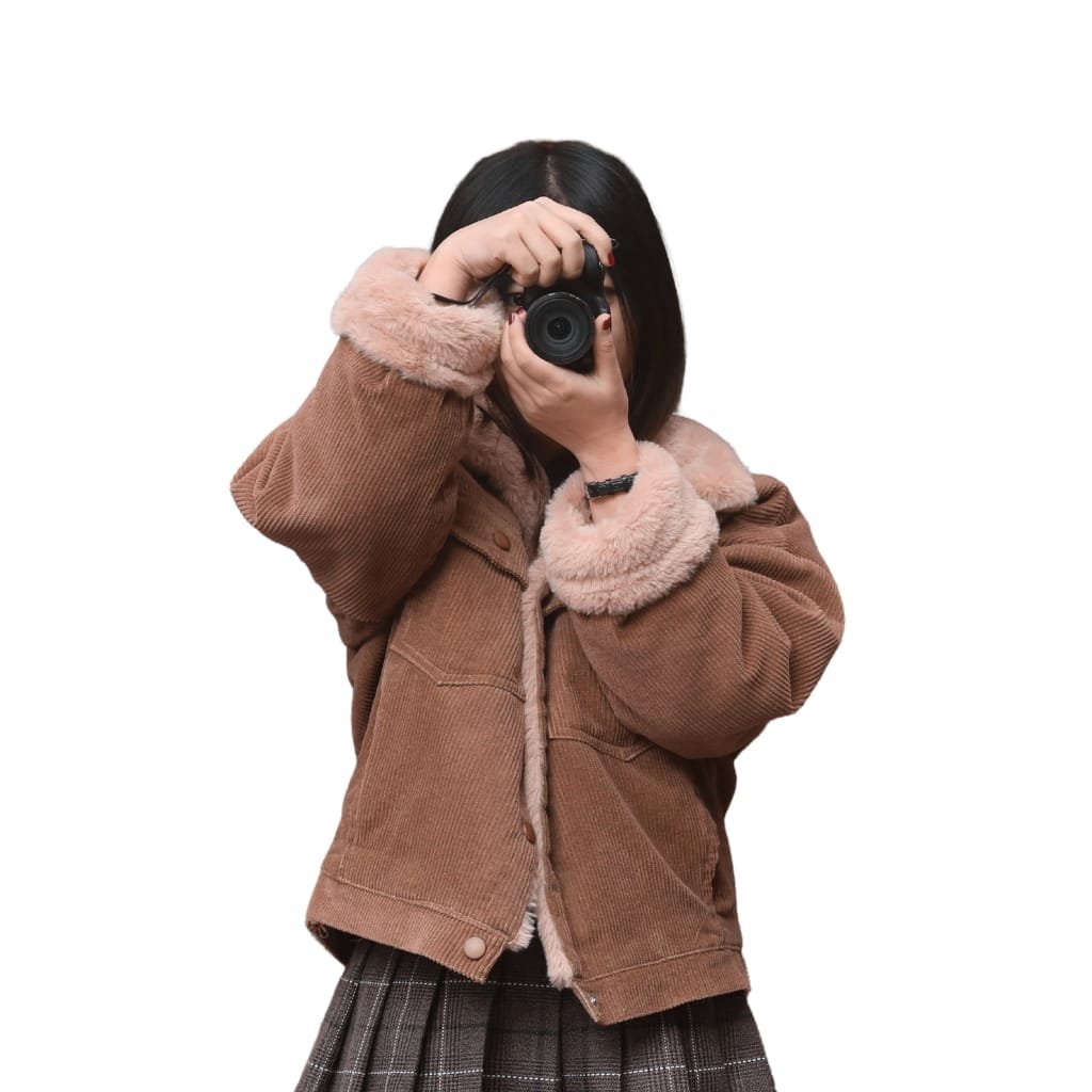 A person wearing a brown corduroy jacket with fluffy collar and cuffs, holding a camera up to their face against a plain white background.