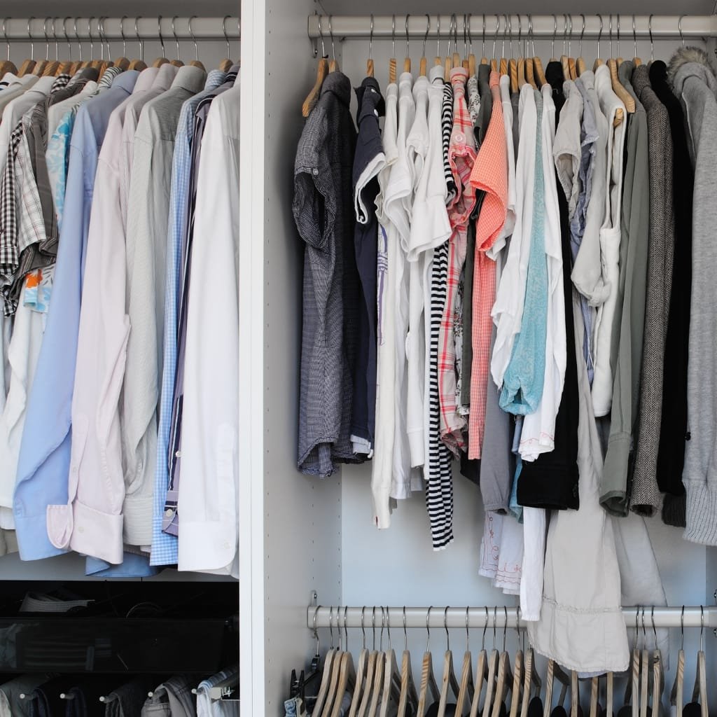 Open closet with neatly arranged shirts, t-shirts, and hoodies on wooden hangers.
