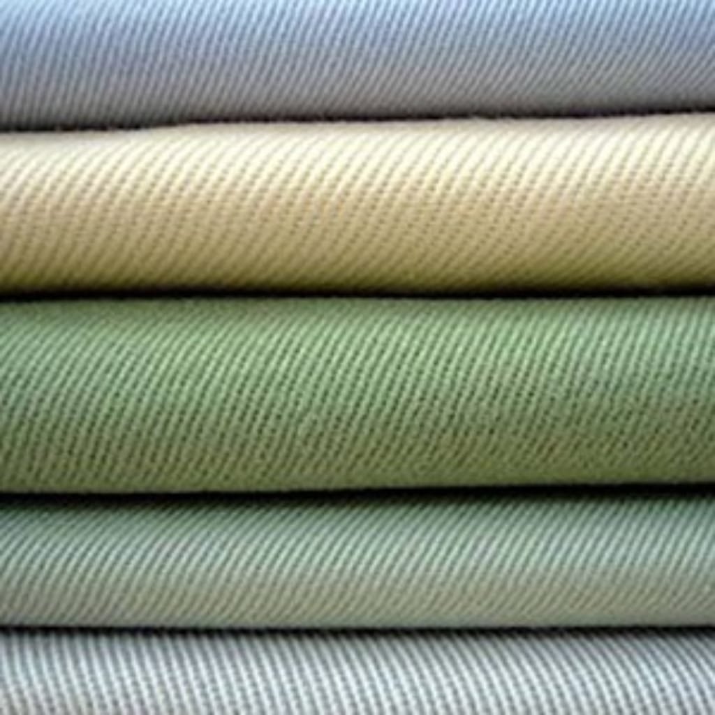 Stacked rolls of fabric in various shades of light green, beige, and gray.