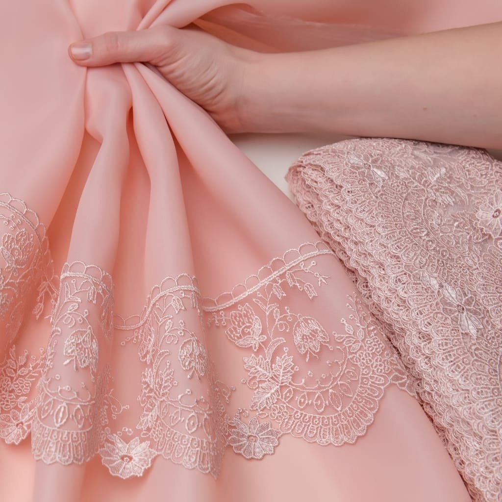 A close-up image of delicate pink crystal organza fabric with intricate embroidery, often used in bridal wear.