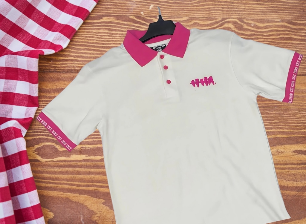 Close-up of a custom embroidered polo shirt with pink accents on the collar and sleeves, displayed on a wooden surface.