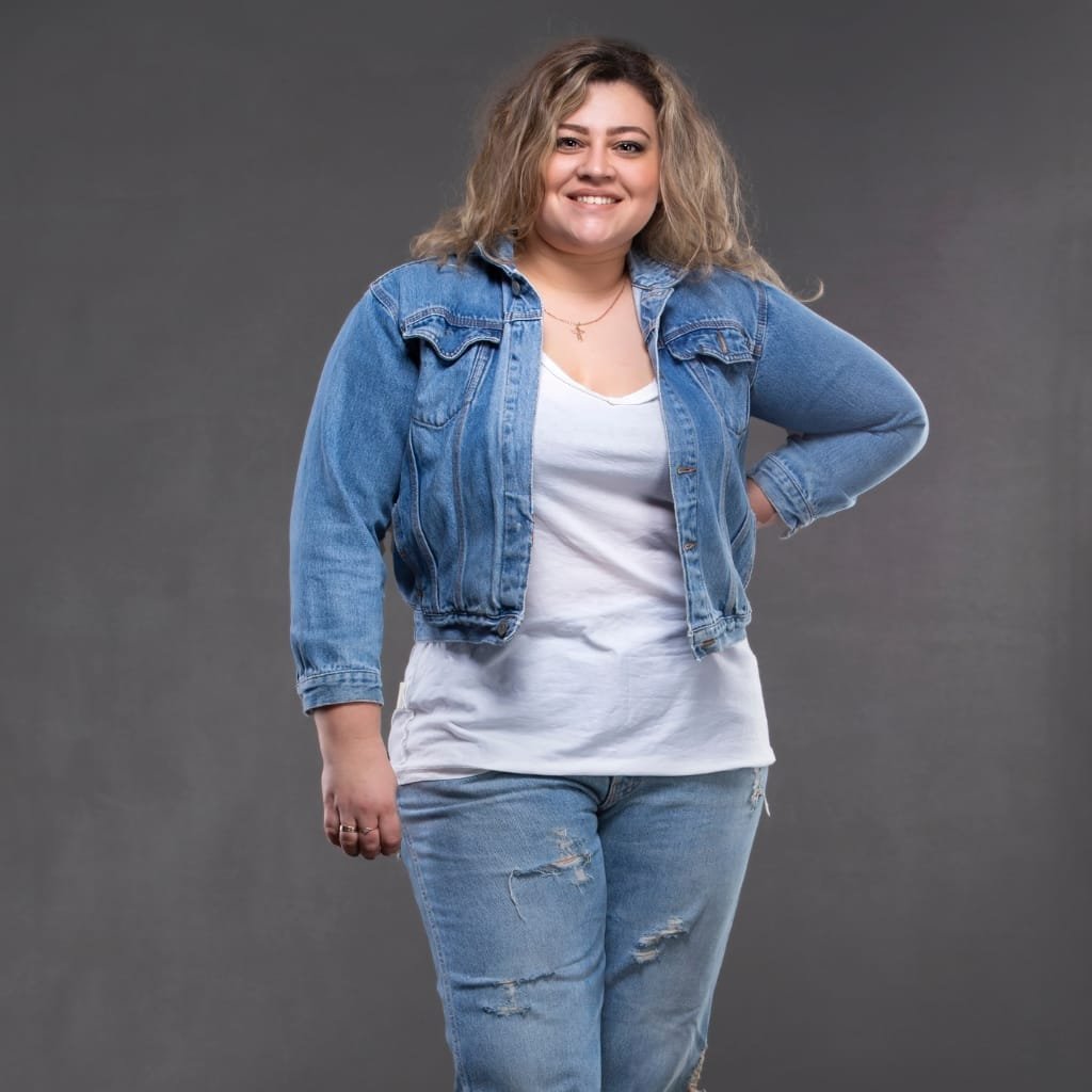 A woman wearing a classic blue denim chambray jacket paired with distressed jeans, smiling confidently against a neutral background.