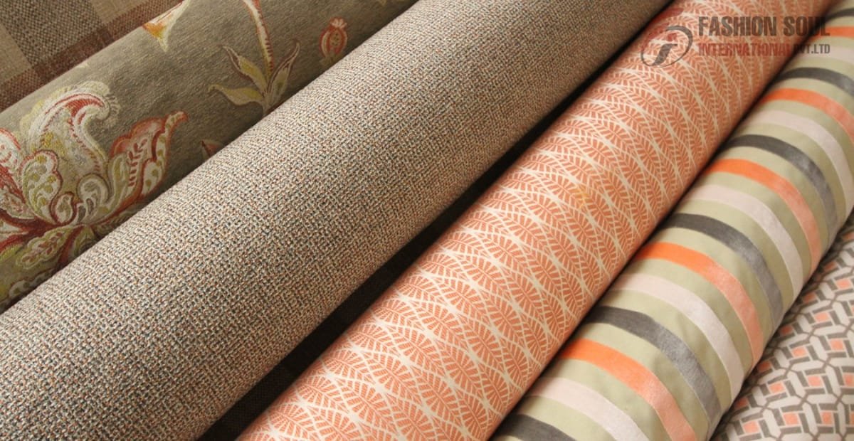 Rolls of patterned fabric with floral, textured, leaf, and geometric designs in neutral, orange, and pastel shades.