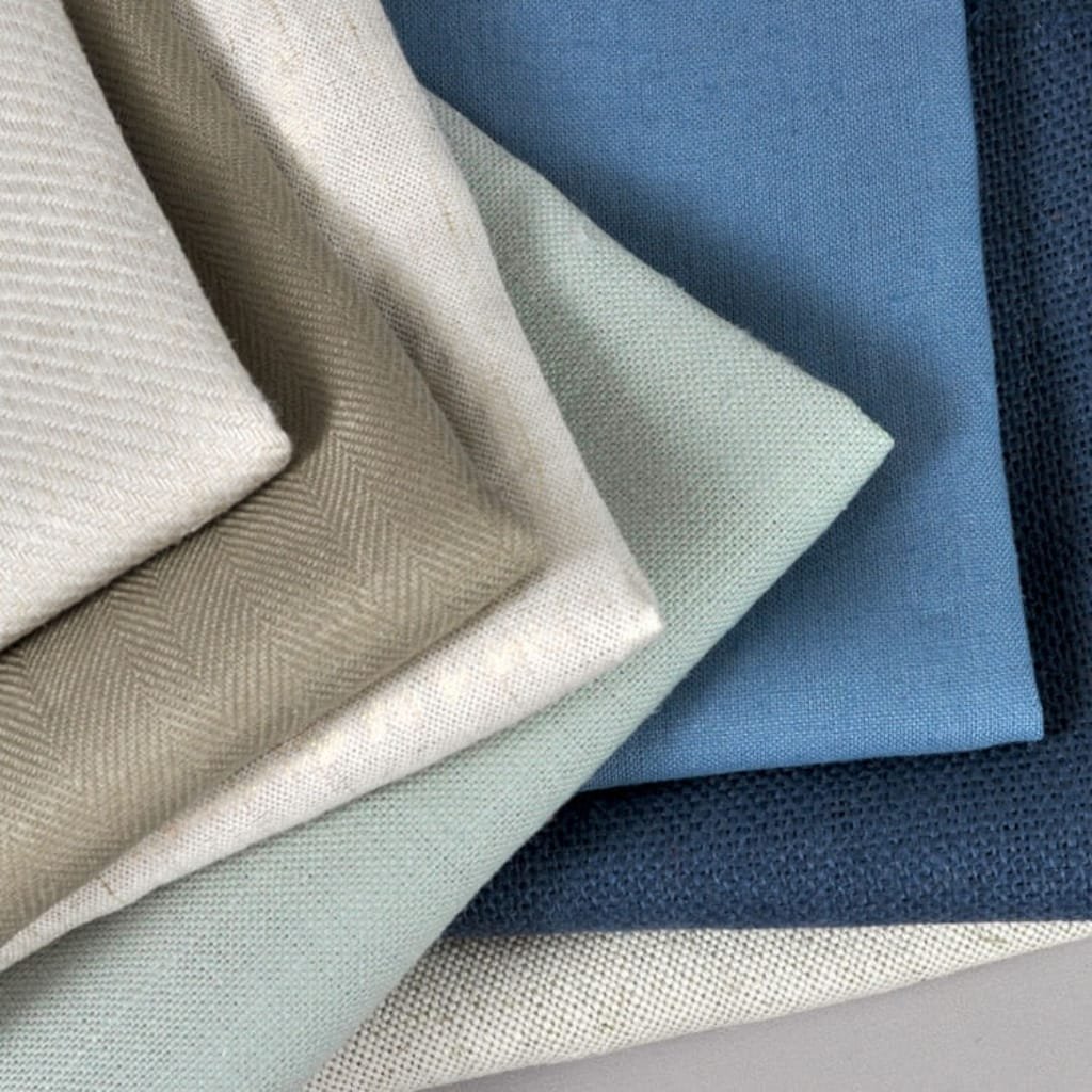 A close-up of multiple folded fabric swatches in neutral and blue tones, showcasing different textures and weaves.