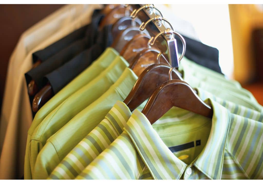 A row of men's polo shirts in various shades of green, beige, and black hanging on wooden hangers on a clothing rack, showcasing different styles and patterns.
