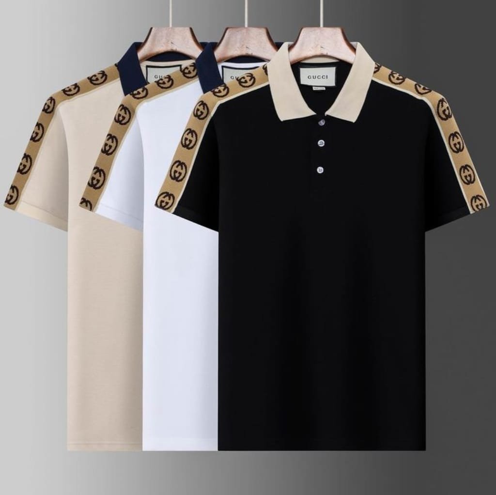 Three Gucci high-fashion polo shirts hanging on wooden hangers, featuring color-block designs with signature Gucci logo tape along the shoulders. The shirts are in beige, white, and black.